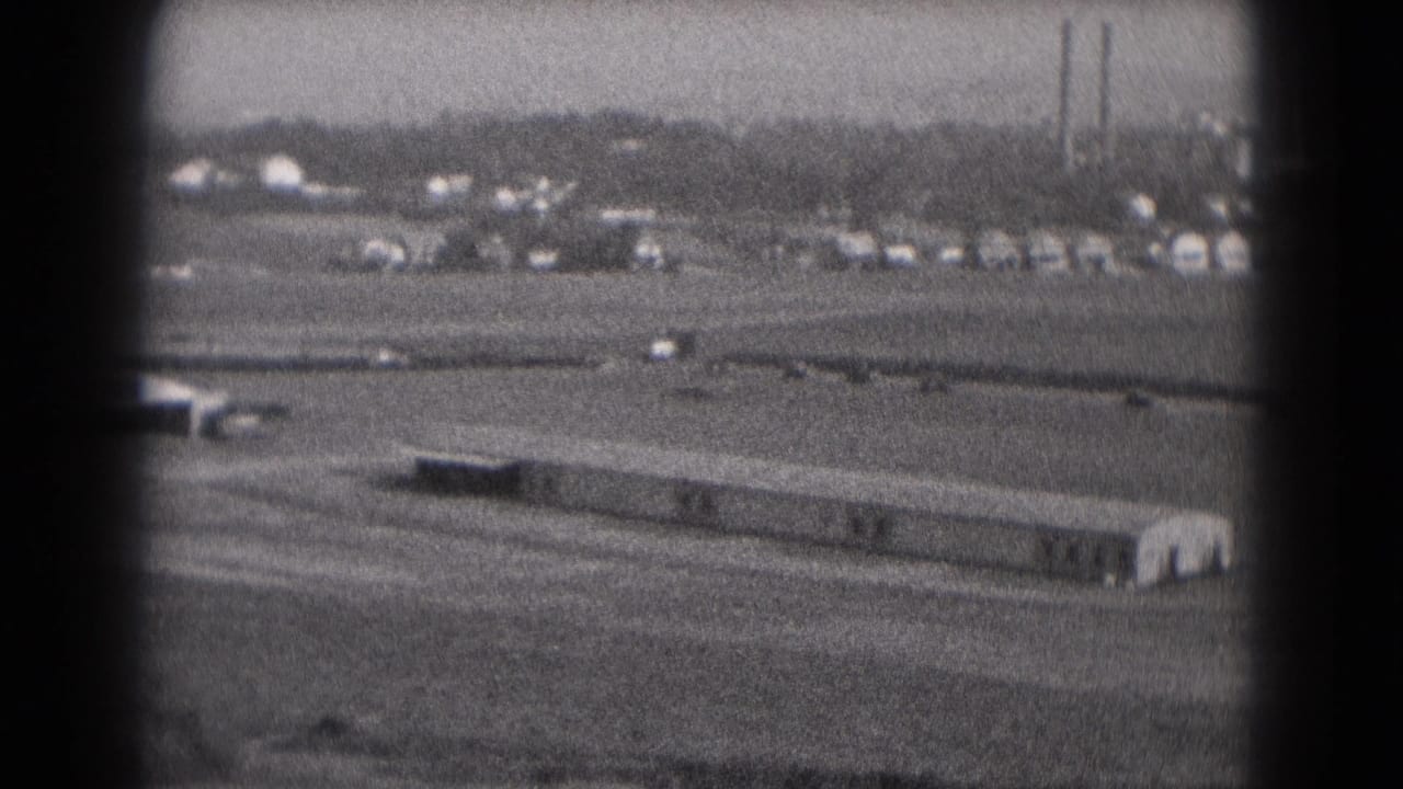 1975 Middletown, Pennsylvania view of vehicles moving behind a long low structure, with trees and factory stacks in the distance.