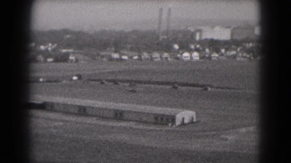 1975 Middletown, Pennsylvania 8mm frame showing the long building and road traffic beneath distant factory smokestacks.