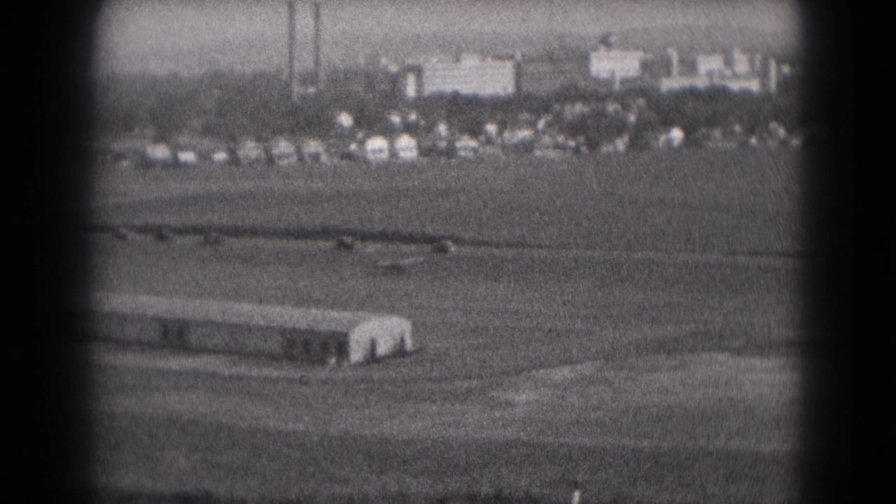 Middletown, Pennsylvania airfield scene from 1975, with a small aircraft moving across the runway area and distant cars and buildings visible.