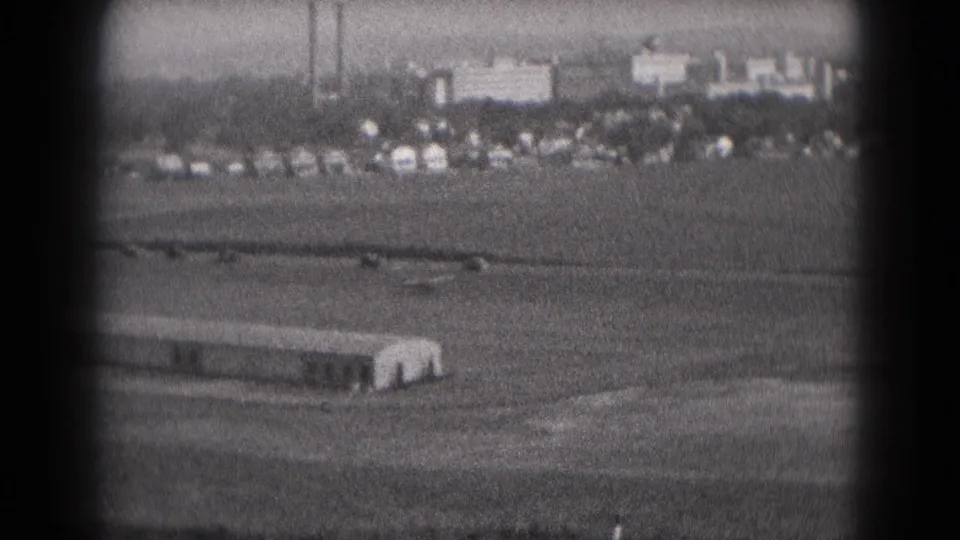Middletown, Pennsylvania airfield scene from 1975, with a small aircraft moving across the runway area and distant cars and buildings visible.