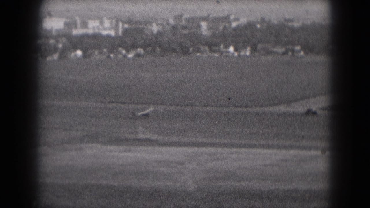 Black-and-white 1975 8mm view near Middletown, Pennsylvania, showing a small airplane moving along a distant rural runway.