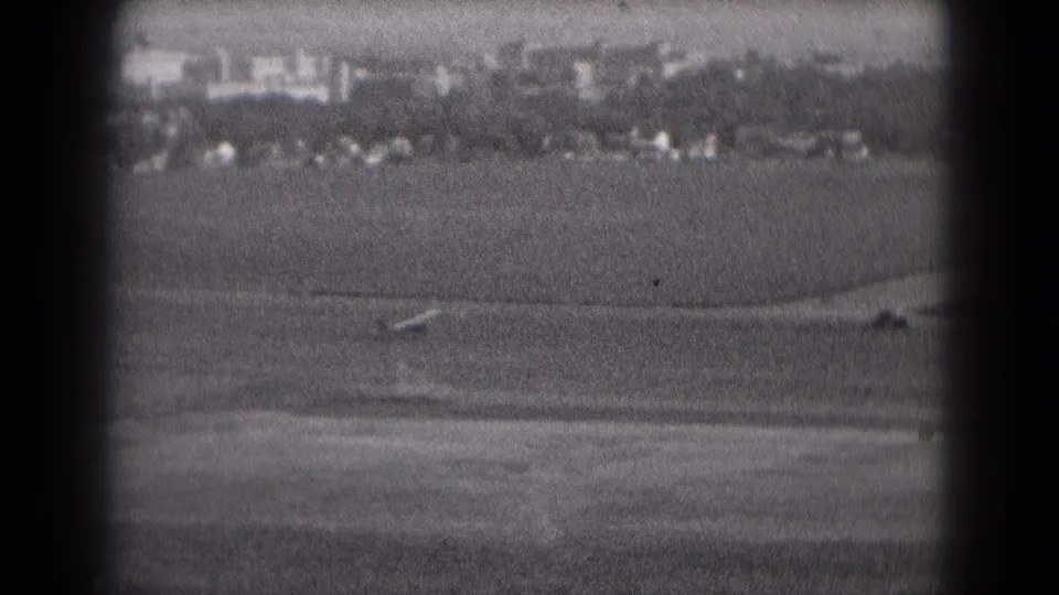 Black-and-white 1975 8mm view near Middletown, Pennsylvania, showing a small airplane moving along a distant rural runway.