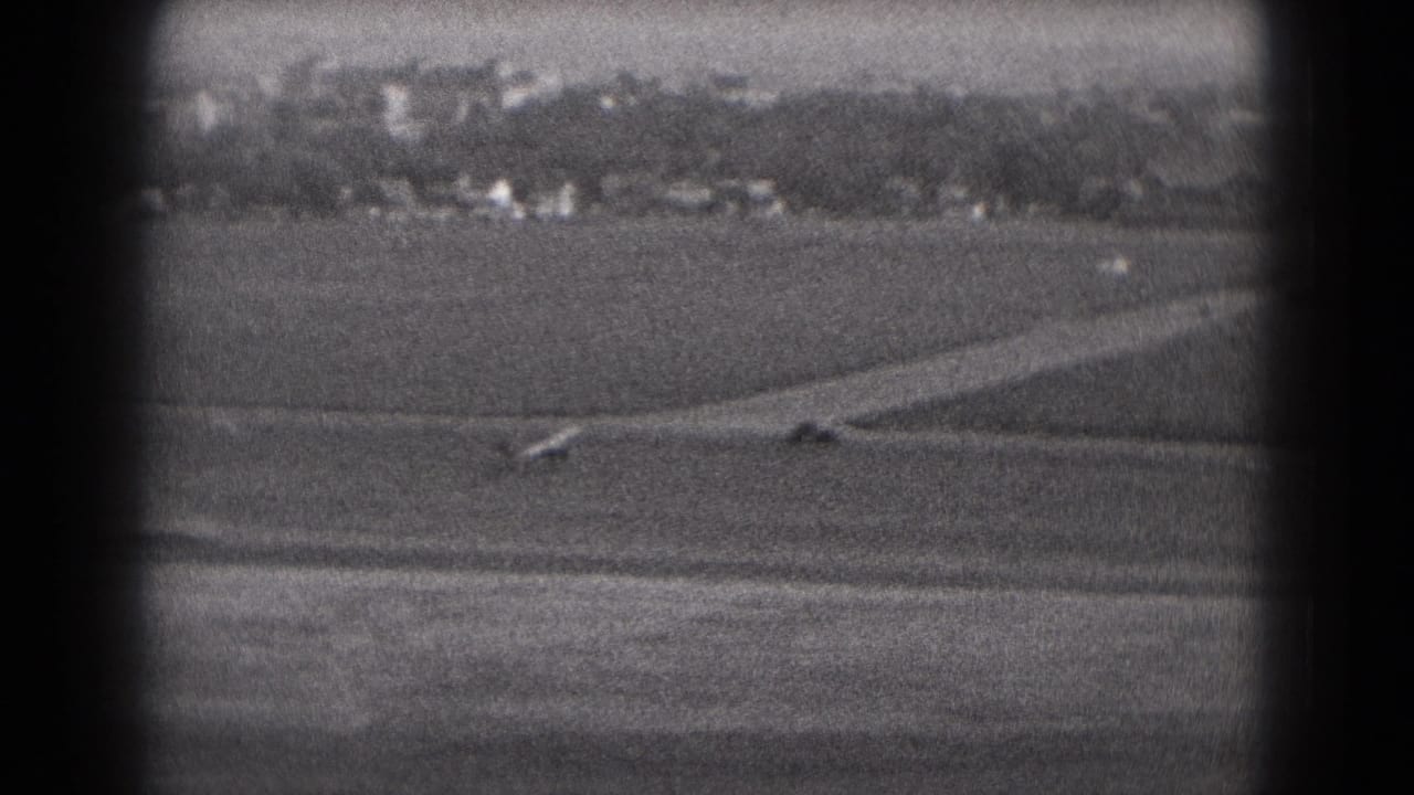 The small aircraft continues across the runway in distant black-and-white 8mm footage from Middletown, Pennsylvania in 1975.