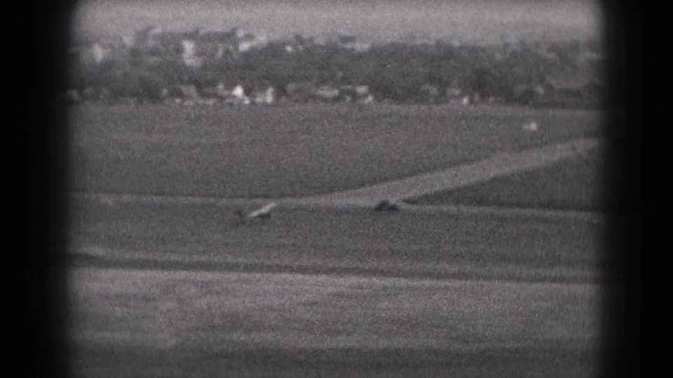 The small aircraft continues across the runway in distant black-and-white 8mm footage from Middletown, Pennsylvania in 1975.