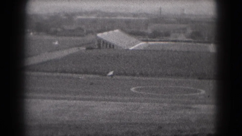 The aircraft appears just above the rural runway area near Middletown, Pennsylvania, captured in grainy black-and-white 8mm film.