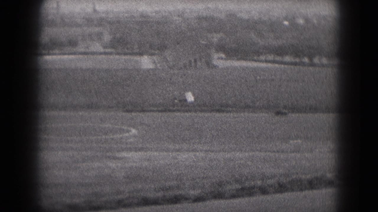 Small airplane moving across a distant runway area with open field behind it.