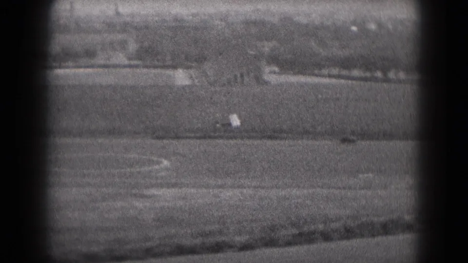 Distant small airplane crossing the rural airfield view in 1975 Middletown, Pennsylvania, with grain and projector vignetting visible.
