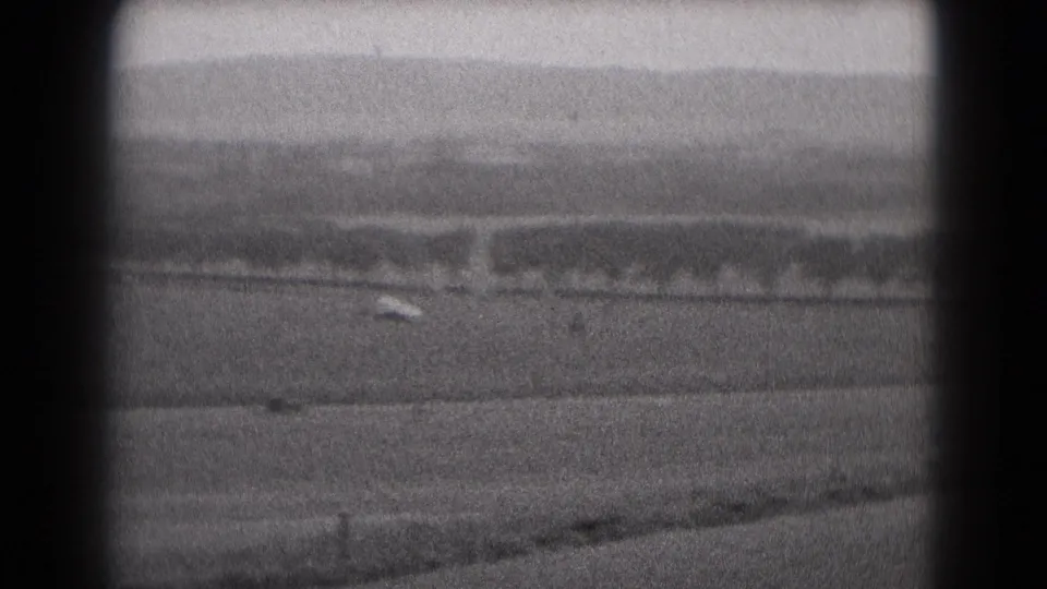 The small airplane is barely visible against a rural Middletown, Pennsylvania airfield scene, recorded on grainy 8mm film in 1975.