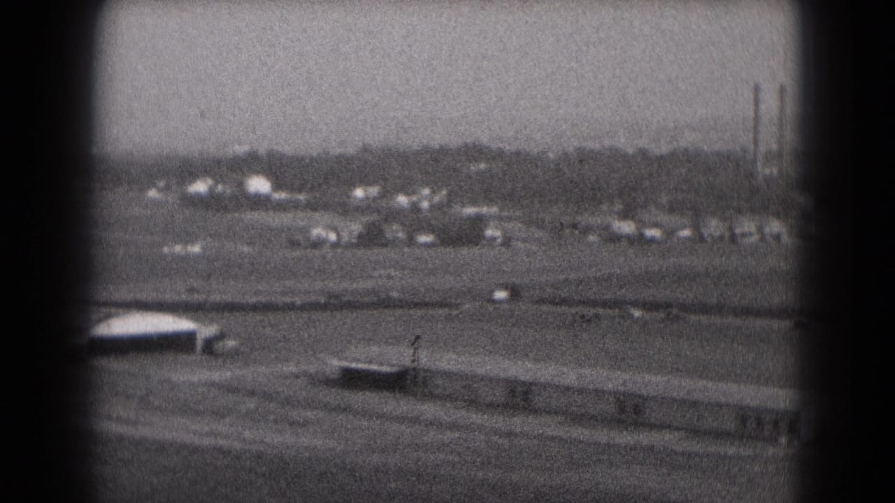 1975 Middletown, Pennsylvania 8mm frame showing an elevated approach view over open airport grounds and distant industrial stacks.
