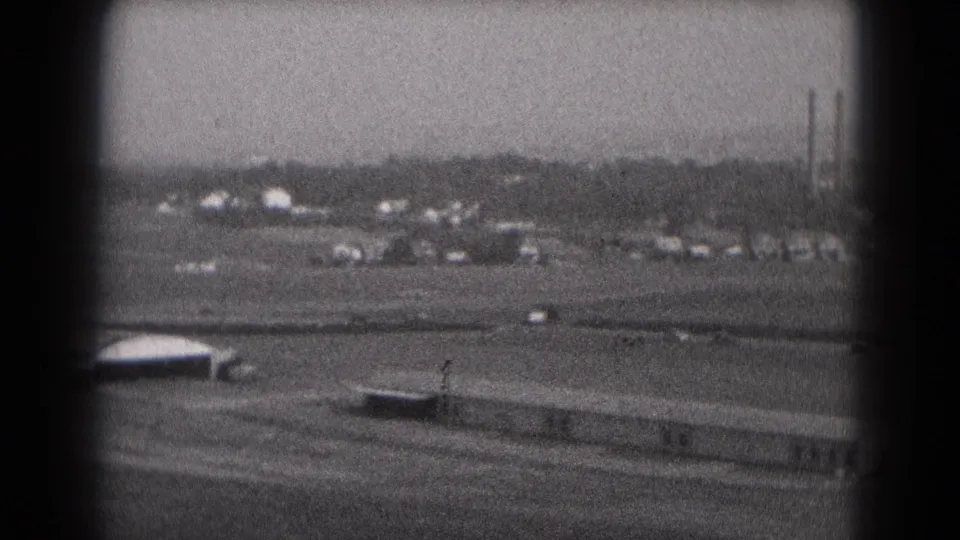 1975 Middletown, Pennsylvania 8mm frame showing an elevated approach view over open airport grounds and distant industrial stacks.