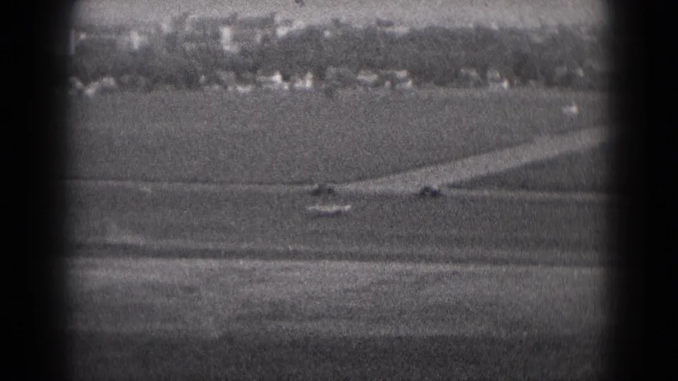 The final 8mm frame shows open ground, a curved paved strip, and distant Middletown-area buildings in soft monochrome.