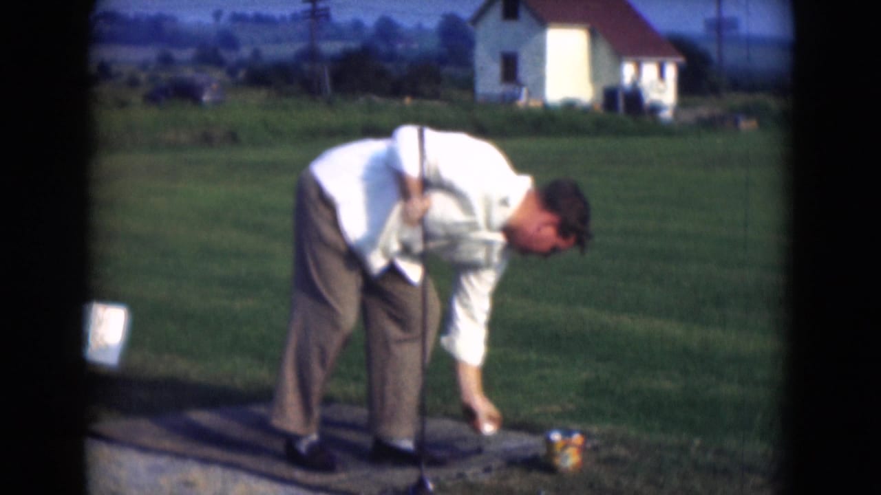 Man bends over to place a golf ball on a tee in a grassy field.