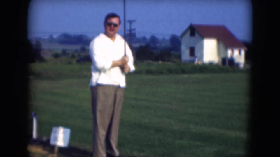 In Middletown, Pennsylvania in 1975, a man in a white shirt and brown trousers stands with a golf club on a grassy field.