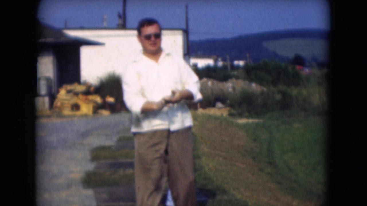 The 1975 Middletown, Pennsylvania home-movie frame shows a man in sunglasses standing with a golf club on grass near a white building.