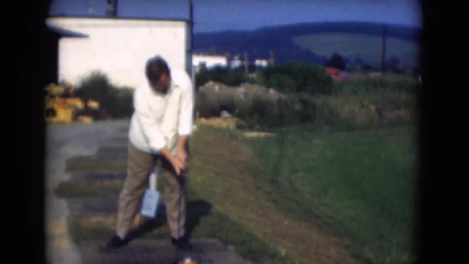 The man bends into a golf swing or putt on grass, with a rural-looking backdrop in 1975 Middletown, Pennsylvania home-movie footage.