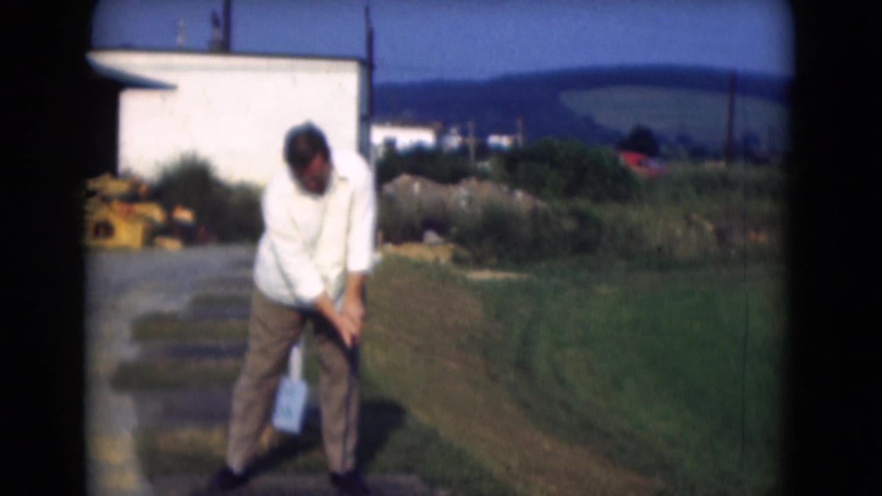 In Middletown, Pennsylvania, 1975, a man in a white shirt and brown trousers sets up for a golf swing on a sunny grassy area.