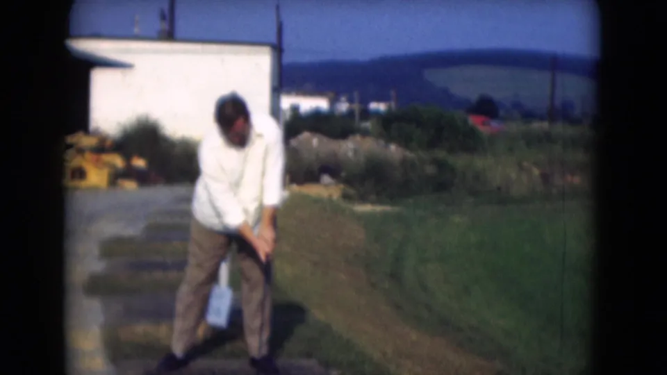 In Middletown, Pennsylvania, 1975, a man in a white shirt and brown trousers sets up for a golf swing on a sunny grassy area.