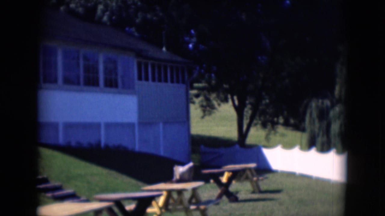 White house beside a green lawn with picnic tables and shaded trees.