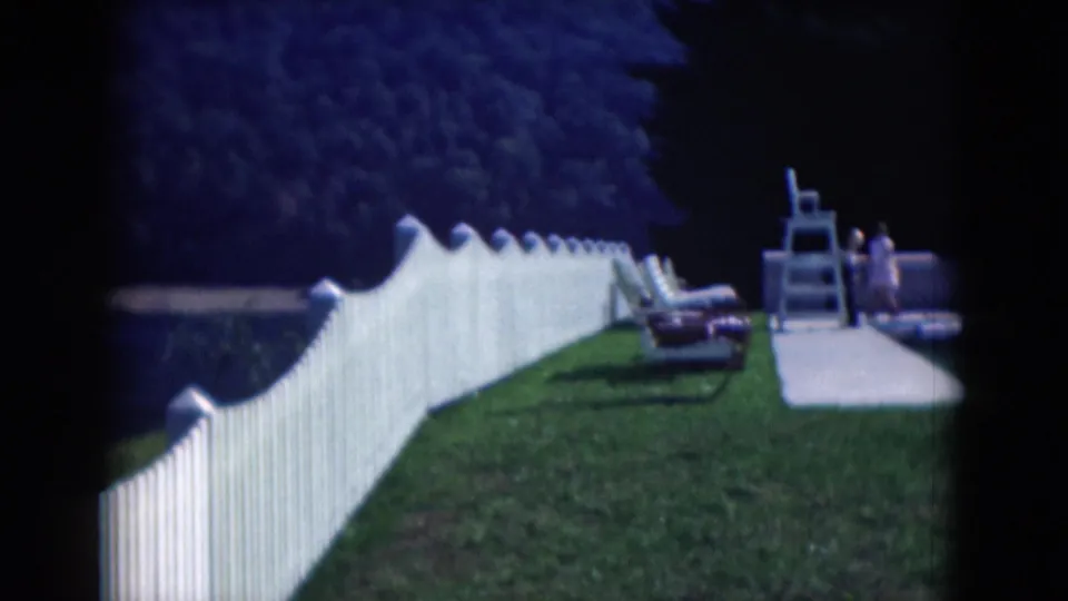 1975 Middletown, Pennsylvania backyard view with a white fence, pool deck, lounge chairs, lifeguard chair, and distant people.