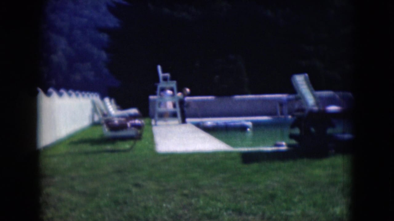 1975 Middletown backyard pool scene with white fence, lawn chairs, walkway, trees, and a distant person near the pool.