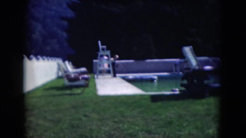 1975 Middletown backyard pool scene with white fence, lawn chairs, walkway, trees, and a distant person near the pool.