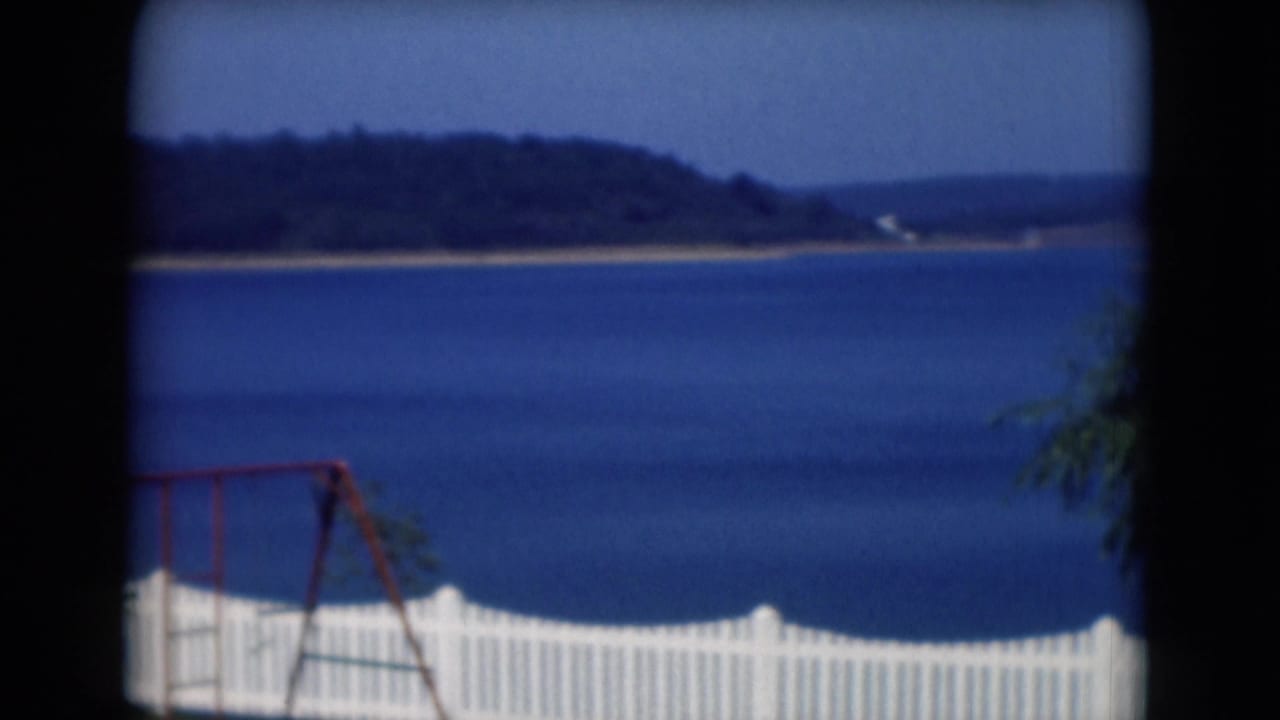 Blue lake beyond a white fence with a red swing set at the edge of the frame.