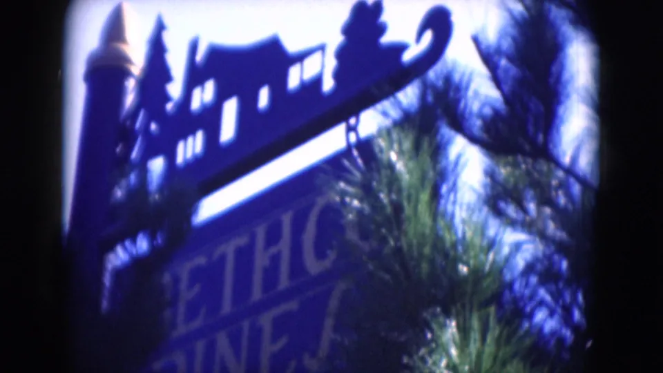 1975 8mm close-up of the Bethco Pines sign, with a silhouetted decorative top rail and pine branches in front.