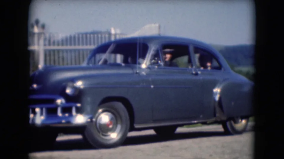 In Middletown, Pennsylvania home-movie footage from 1975, a blue sedan moves left to right past a fence with people visible inside.