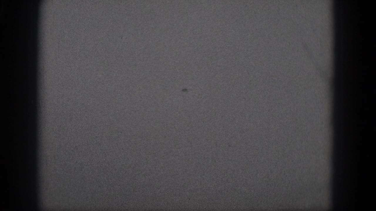 1975 8mm frame from Middletown metadata showing grain, dark borders, and an indistinct light gray field.