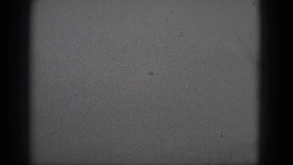 Grainy 8mm frame with dark gate edge shapes and no identifiable people, objects, or setting.