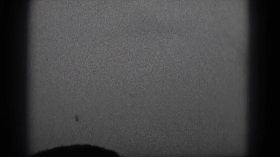 1975 8mm frame from supplied Middletown metadata with grain, black borders, and an indistinct dark form at the lower edge.