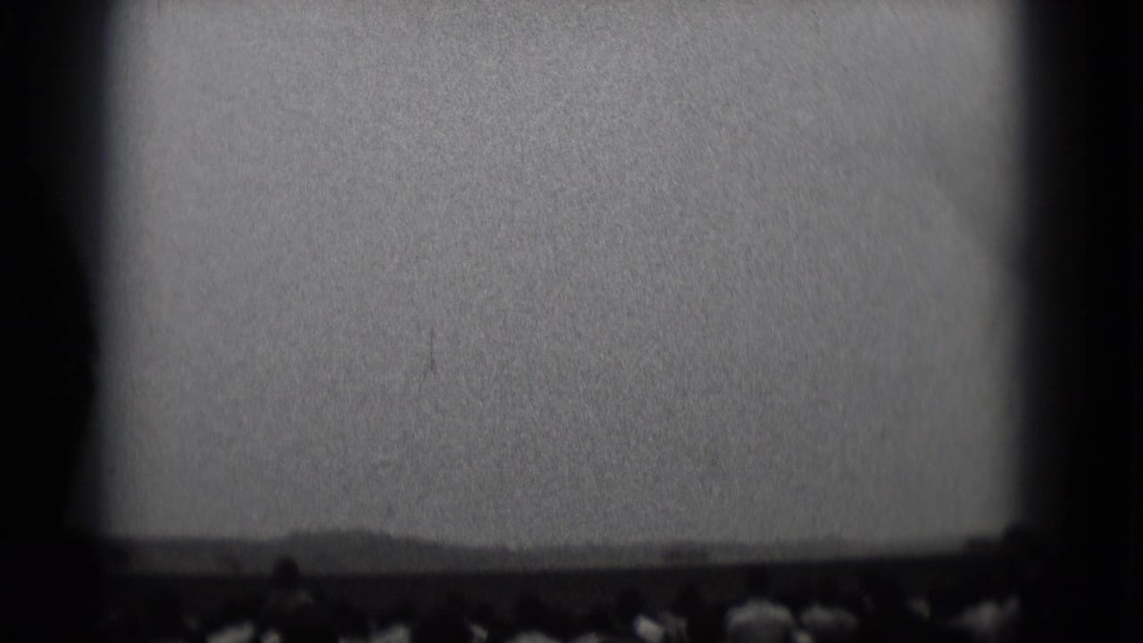 Silhouetted crowd seen below a bright sky or screen area with dark film edges.