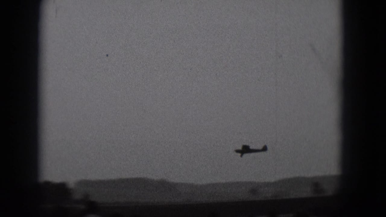 Small propeller airplane silhouetted against a hazy sky above a faint horizon.