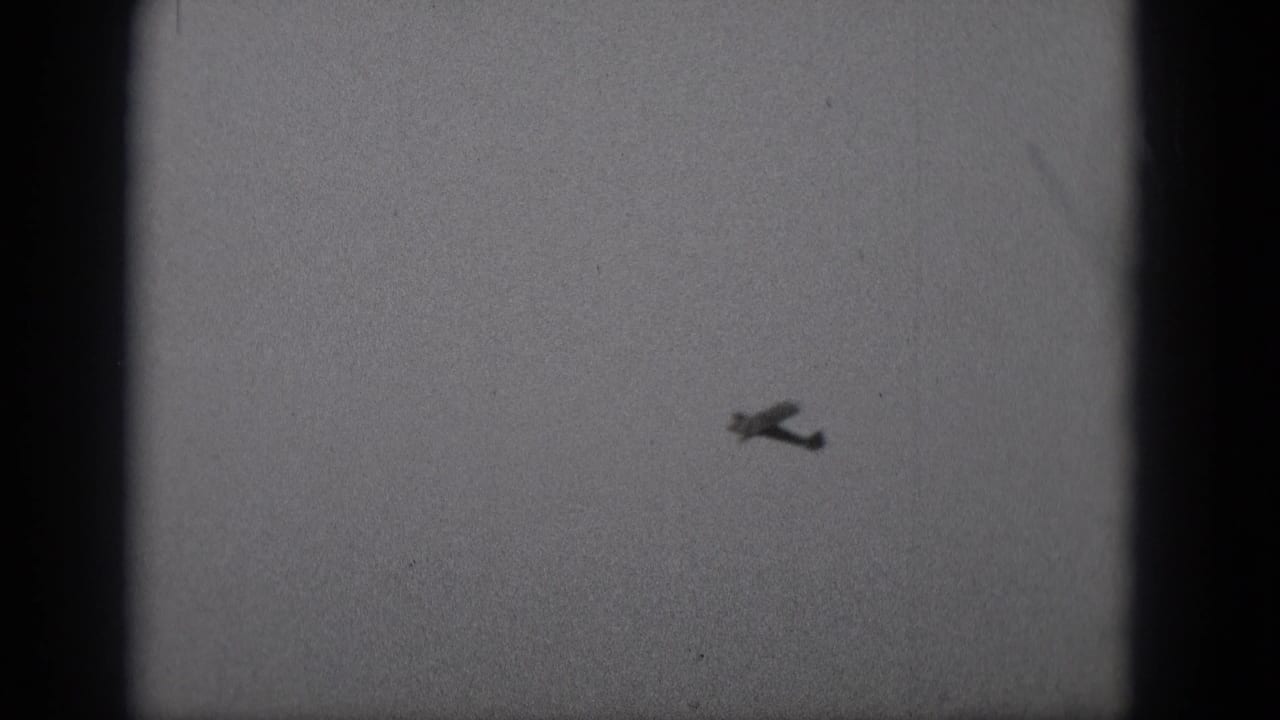 Small airplane silhouette centered high in a pale grainy sky.