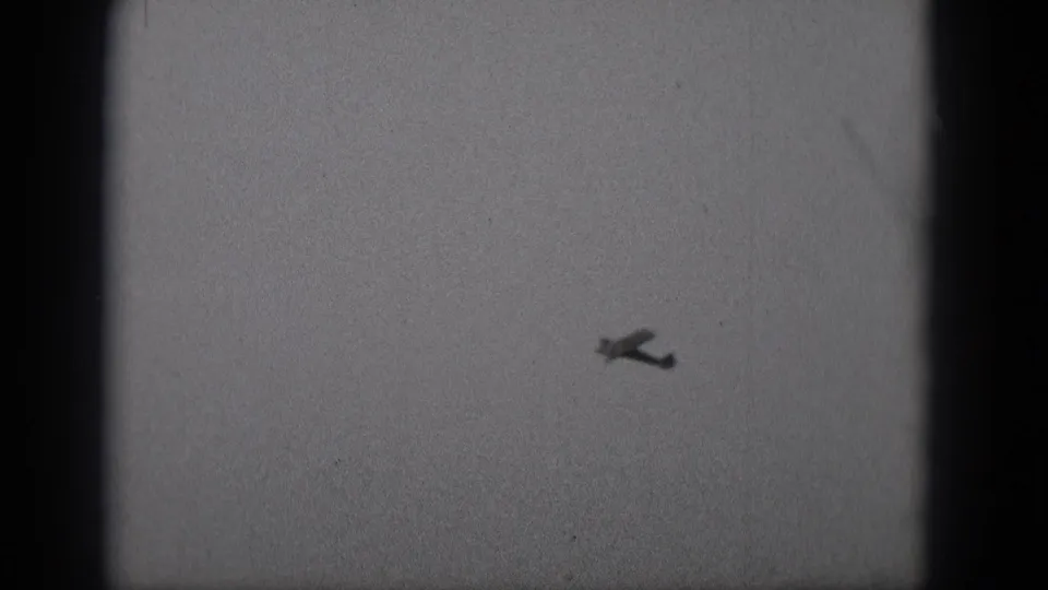 1975 Middletown, Pennsylvania 8mm frame with a small propeller airplane silhouetted in a pale, grainy sky.