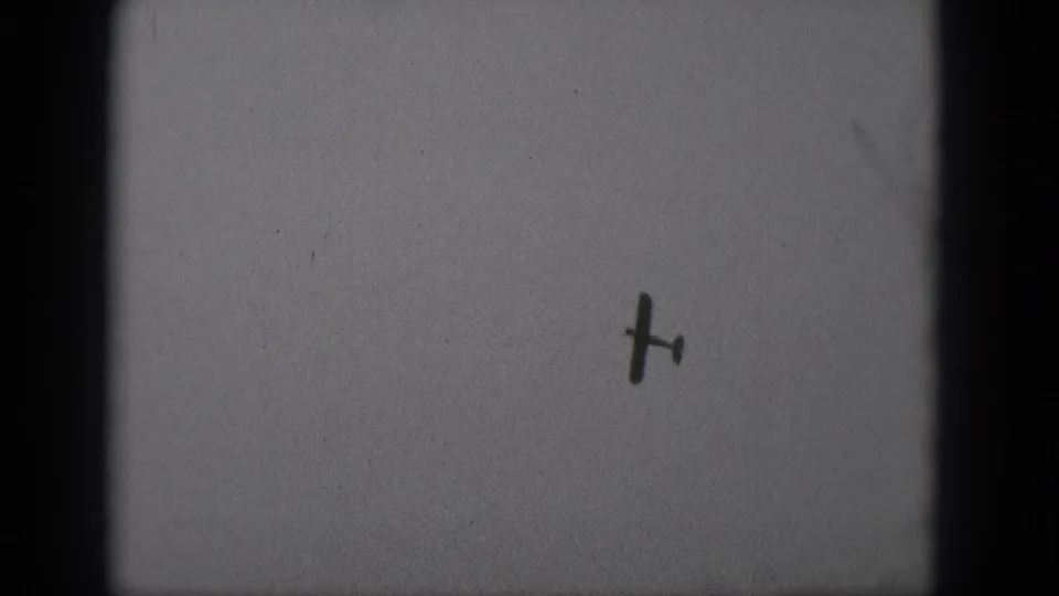 1975 Middletown, Pennsylvania 8mm frame showing the airplane from below as a dark shape against gray sky.
