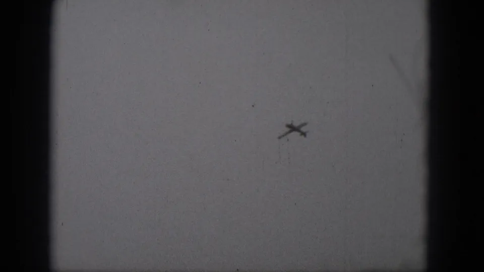 1975 Middletown, Pennsylvania 8mm frame of a distant airplane angled across a hazy sky within visible film-frame edges.