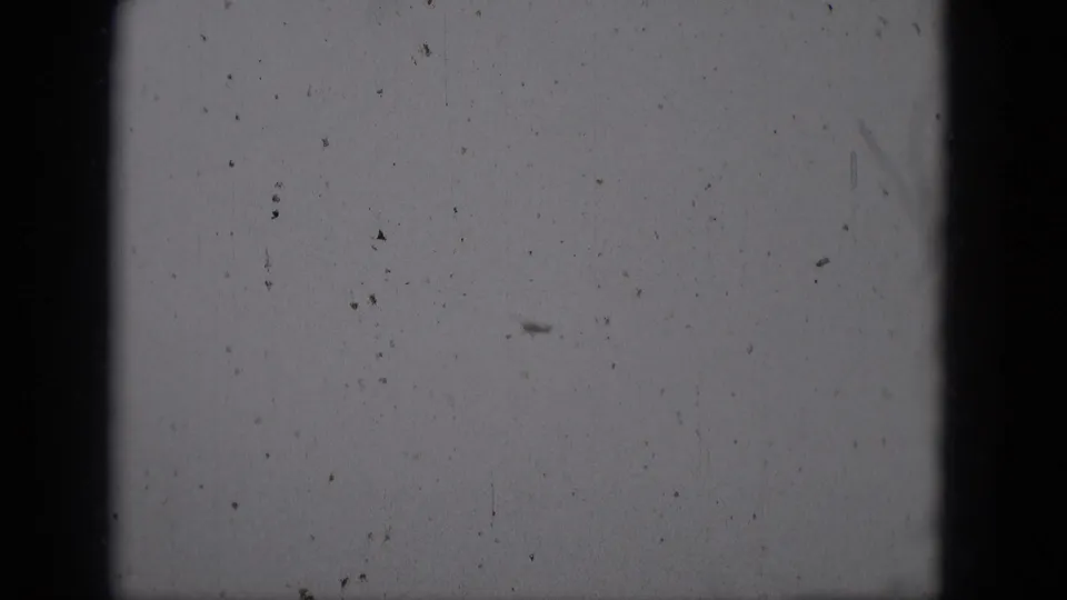 The aircraft remains distant in the 1975 Middletown 8mm footage, crossing a blank overcast sky amid dust and grain.