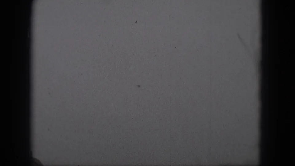 A sparse 1975 8mm sky frame from Middletown shows mostly blank overcast sky and physical film texture as the aircraft fades from view.