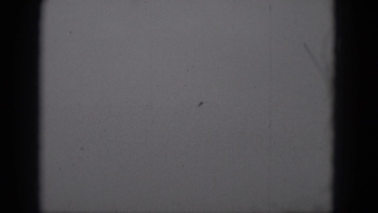 1975 Middletown, Pennsylvania 8mm frame showing a small airplane silhouette high against a pale monochrome sky.