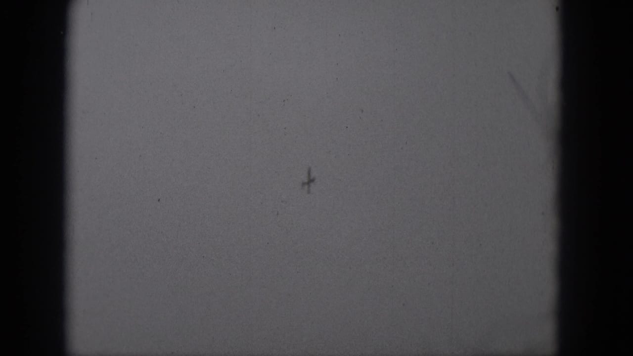 Black-and-white 8mm frame from Middletown metadata showing a distant aircraft shape near the upper right sky area.