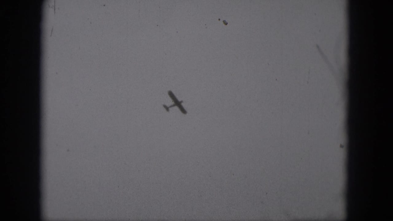Small aircraft tilted in flight against a blank gray sky.
