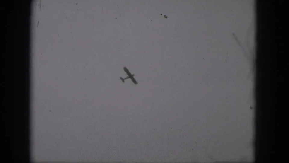 A small airplane is seen tilted in flight against an open gray sky in this 1975 8mm Middletown, Pennsylvania frame.