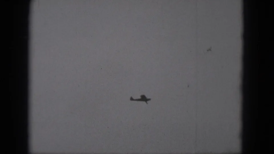 A small airplane appears as a dark silhouette against an overcast sky in this 1975 Middletown, Pennsylvania 8mm frame.