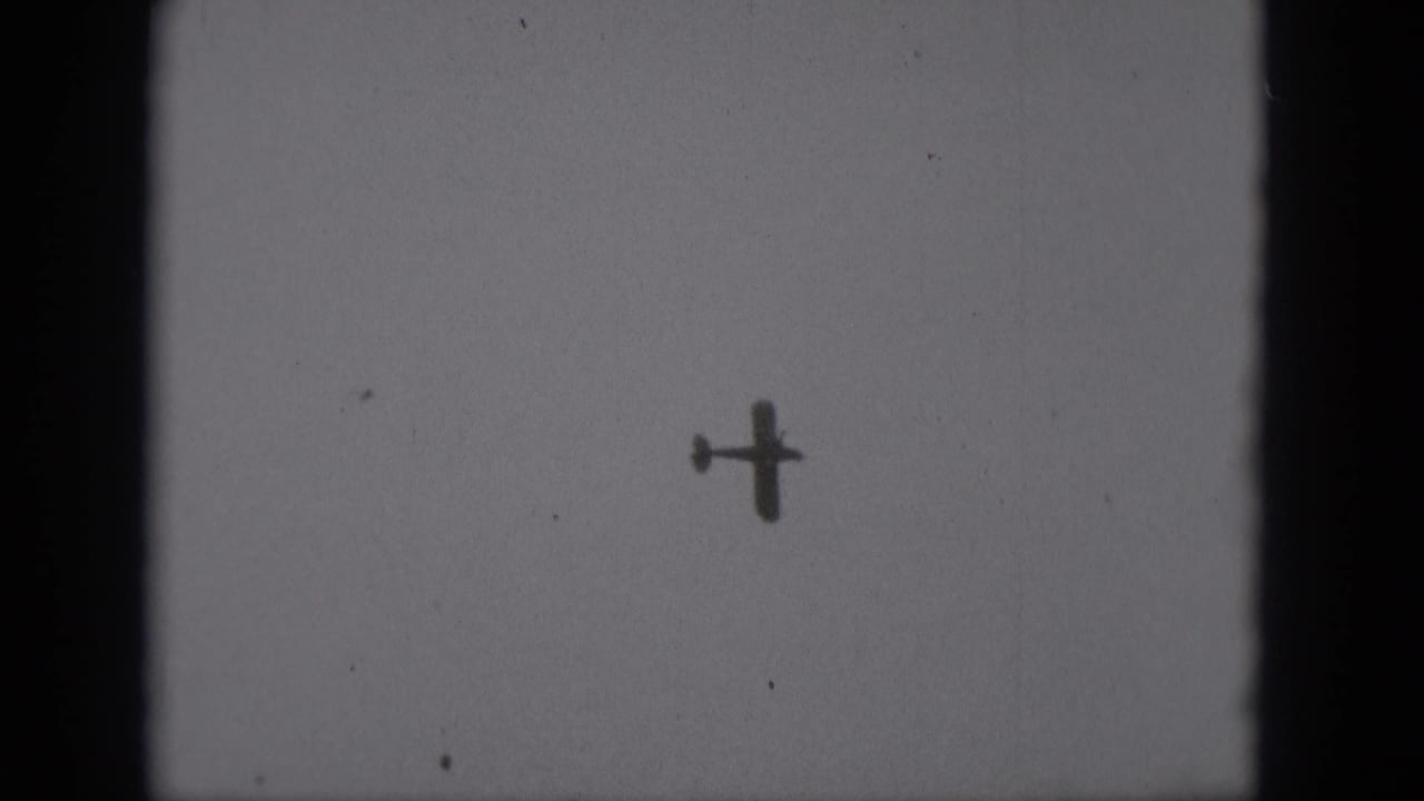 Distant airplane silhouette higher in the sky with visible grain and frame borders.