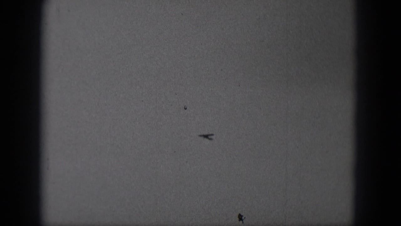 Distant small airplane silhouetted in the sky in 1975 Middletown, Pennsylvania home-movie footage.