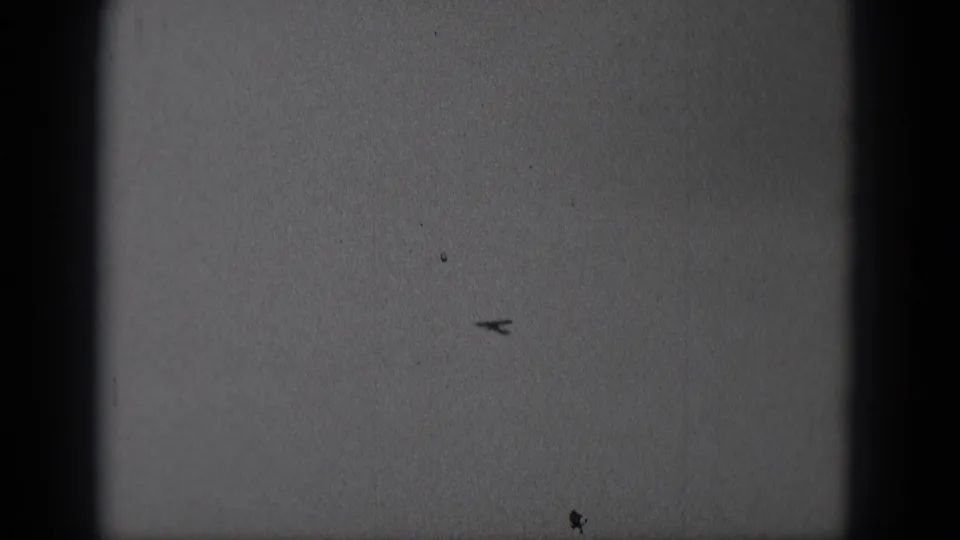 Distant small airplane silhouetted in the sky in 1975 Middletown, Pennsylvania home-movie footage.