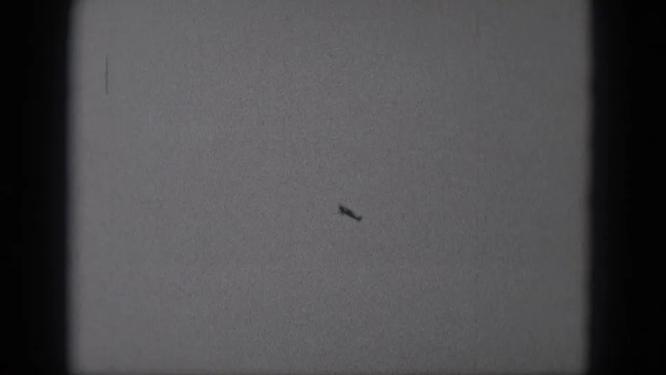 A distant aircraft silhouette sits low in the 8mm frame, with visible grain and dark gate edges.
