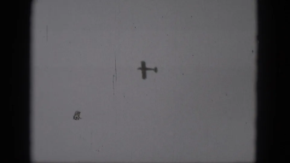 A small plane silhouette appears lower in the frame, with 8mm grain and dust visible in the sky area.