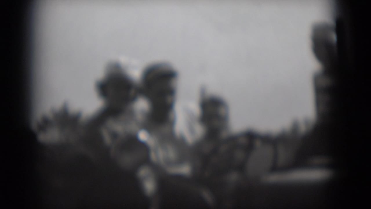 Soft black-and-white frame of several adults gathered outdoors with dark film borders.